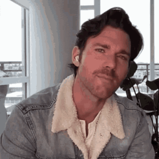 a man wearing a denim jacket with a fur collar and ear buds .