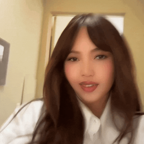 a woman with long brown hair wearing a white shirt is smiling