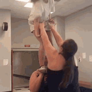a girl is being lifted in the air by a man in a gym .