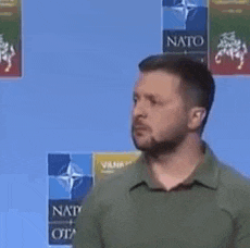 a man with a beard and a green shirt is standing in front of a blue background .