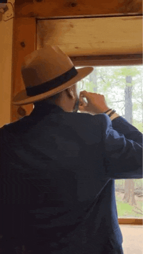 a man wearing a hat and a blue jacket is looking out a window