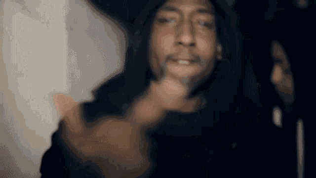 a man in a hooded jacket is pointing at the camera while a woman looks on .