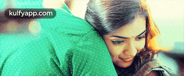 a woman is hugging a man in a green shirt with polka dots .