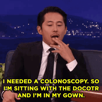 a man in a suit and tie is sitting in a chair with his hand to his mouth and says he needed a colonoscopy .