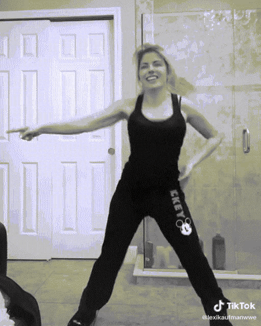 a woman in a black tank top and black mickey mouse sweatpants dancing