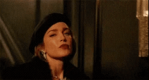 a woman wearing a beret and a necklace is standing next to a man in a suit .
