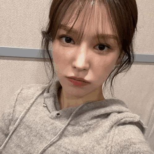 a close up of a woman taking a selfie with a gray hoodie on .