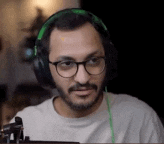 a man with glasses and headphones is sitting in front of a computer screen .
