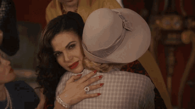 a woman with red nails is hugging another woman in a hat