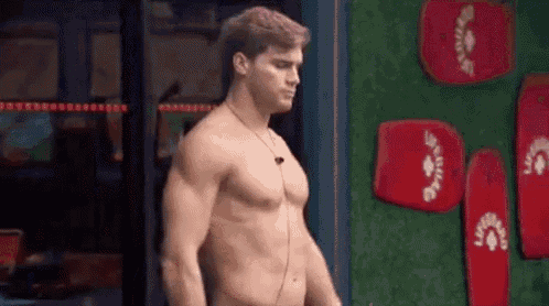 a shirtless man is standing in front of a wall with red surfboards .