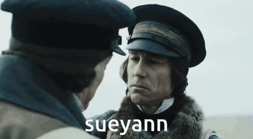 a man in a hat talks to another man with the name sueyann on the bottom