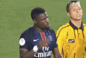 a soccer player wearing a fly emirates jersey is standing next to a referee