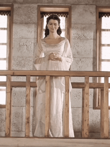 a woman in a white dress is standing on a wooden railing