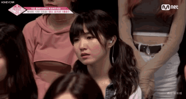 a group of girls are sitting in a room and one of them is wearing a pink crop top