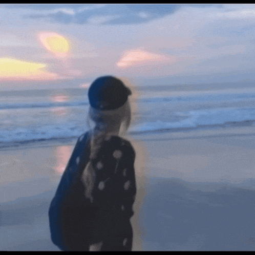 a girl in a black hat stands on a beach
