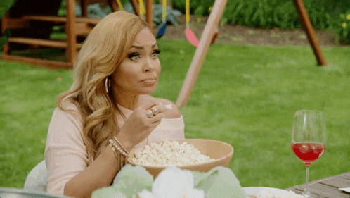 a woman sitting at a table eating popcorn and drinking wine