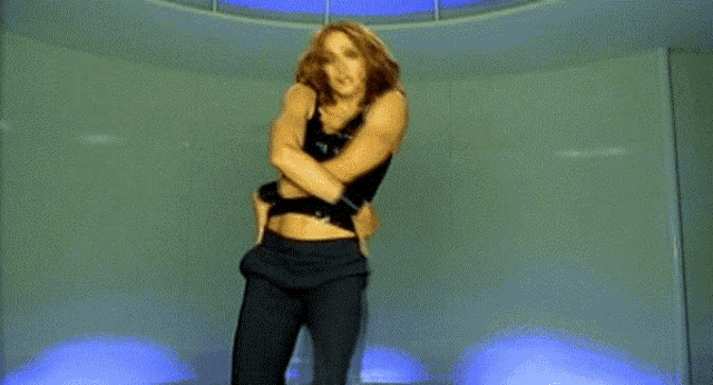a woman in a black bra and black pants is dancing in a room with blue lights .