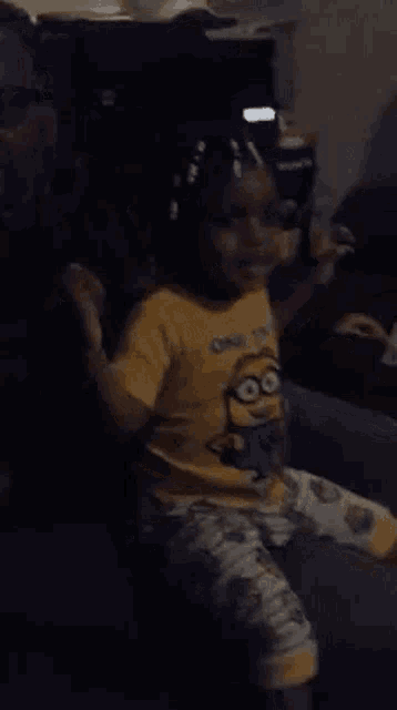 a little girl wearing a yellow minion shirt is sitting on a couch with a man .
