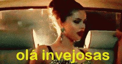 a woman is sitting in a car with a knife in her mouth and the words ola invejosas written on the screen .