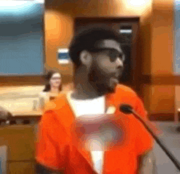 a man in an orange jumpsuit is speaking into a microphone .