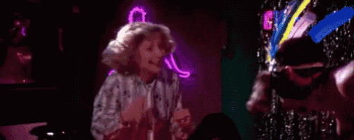 a woman is singing into a microphone in a dark room with a neon sign in the background .