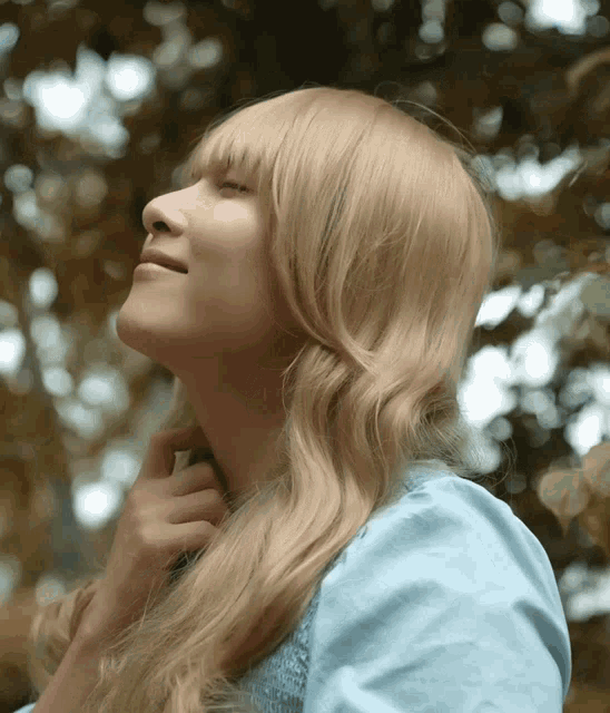 a woman with blonde hair and a blue shirt looks up at the sky
