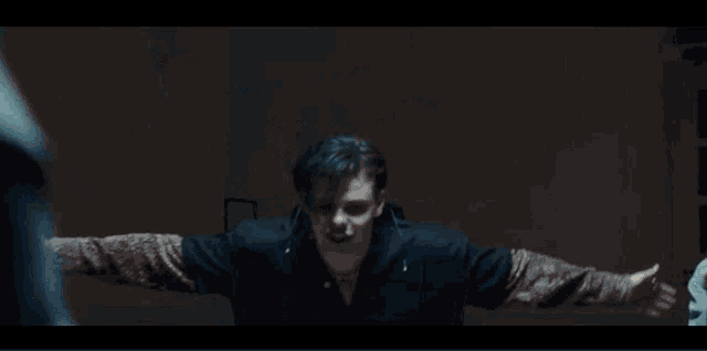 a man in a black jacket stands in a dark room with smoke coming out of the ceiling