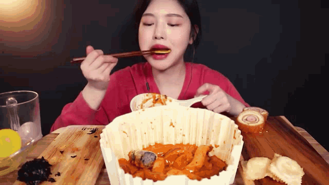 a woman in a red shirt is eating food with chopsticks and a spoon
