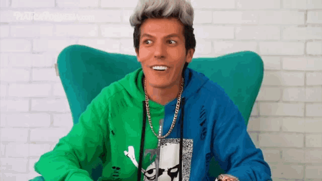 a man wearing a green and blue hoodie sits in a blue chair