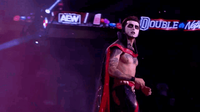 a wrestler wearing a day of the dead mask and a red cape is walking into a ring .