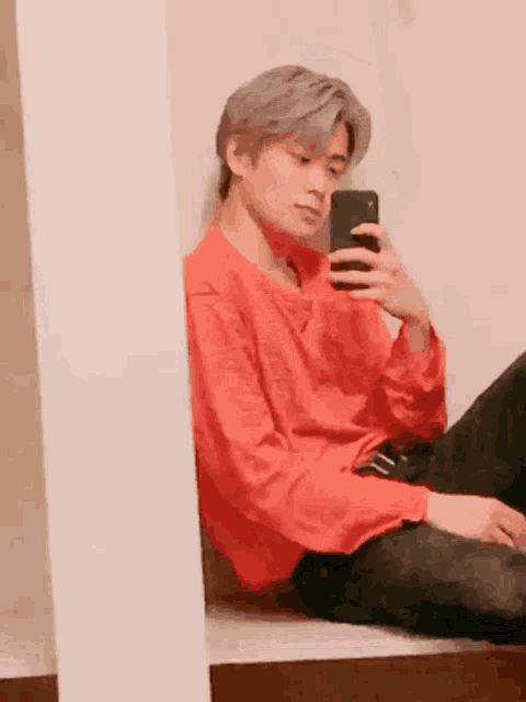 a young man in a red shirt is taking a selfie with his phone .
