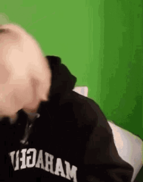 a man wearing a black hoodie is sitting on a bed in front of a green wall .