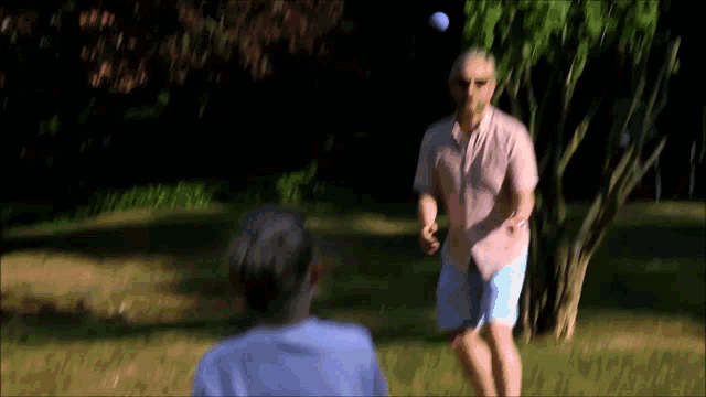 a man in a pink shirt throws a golf ball to another man