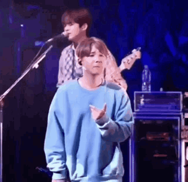 a man in a blue sweater is standing on a stage with a microphone .