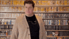 a man in a tan cardigan stands in front of a shelf full of video games