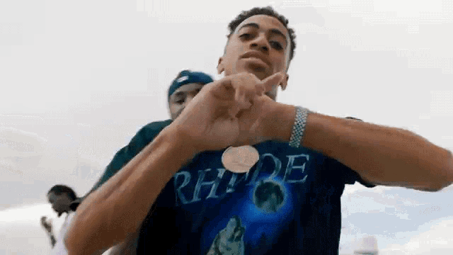 a young man wearing a t-shirt with the word rhde on it is making a heart shape with his hands .