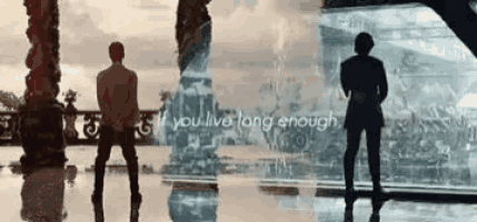 two men are standing next to each other in front of a large screen with the words `` if you live long enough '' .