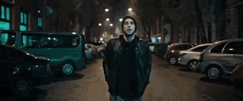 a man in a hooded jacket stands on a street at night