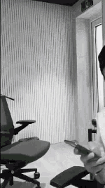 a black and white photo of a person sitting in an office chair looking at their phone