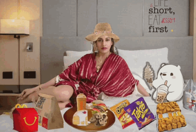 a woman is sitting on a bed surrounded by food including cheetos and takis