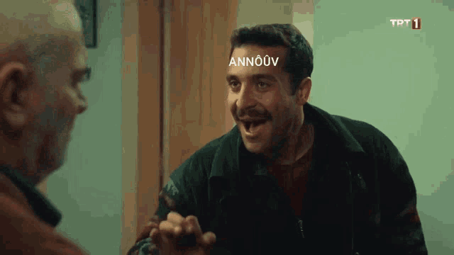 a man with a mustache is talking to another man with trt1 written on the bottom