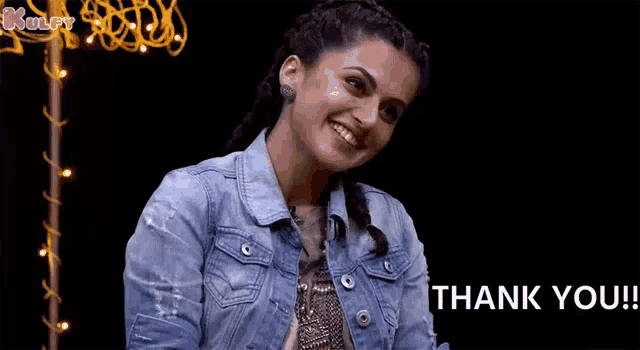 a woman in a denim jacket is giving a thank you sign .