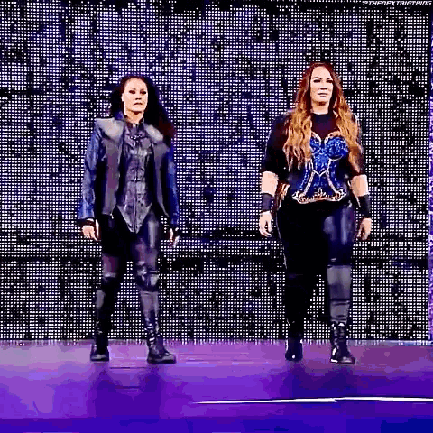 two women are standing next to each other on a stage in front of a large screen .