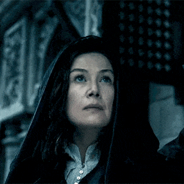 a woman wearing a black hooded cloak looks up at the sky