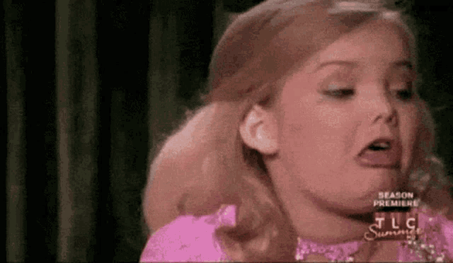 a little girl in a pink dress is making a funny face with her mouth open .