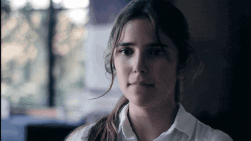 a woman in a white shirt looks at the camera with a sad look on her face