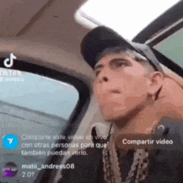 a man is sitting in a car wearing a hat and a necklace .