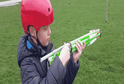 a young boy wearing a red helmet is holding a green toy gun
