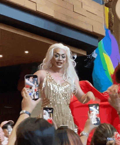 a drag queen in a gold dress is being photographed by a crowd of people