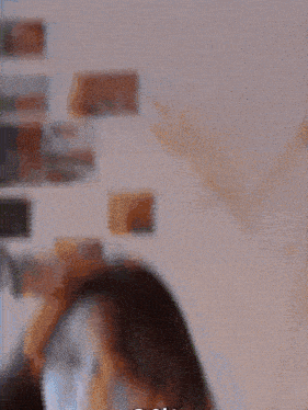 a close up of a woman 's face with a blurred background and a few images on the wall